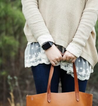 woman standing holding a brown leather tote bag